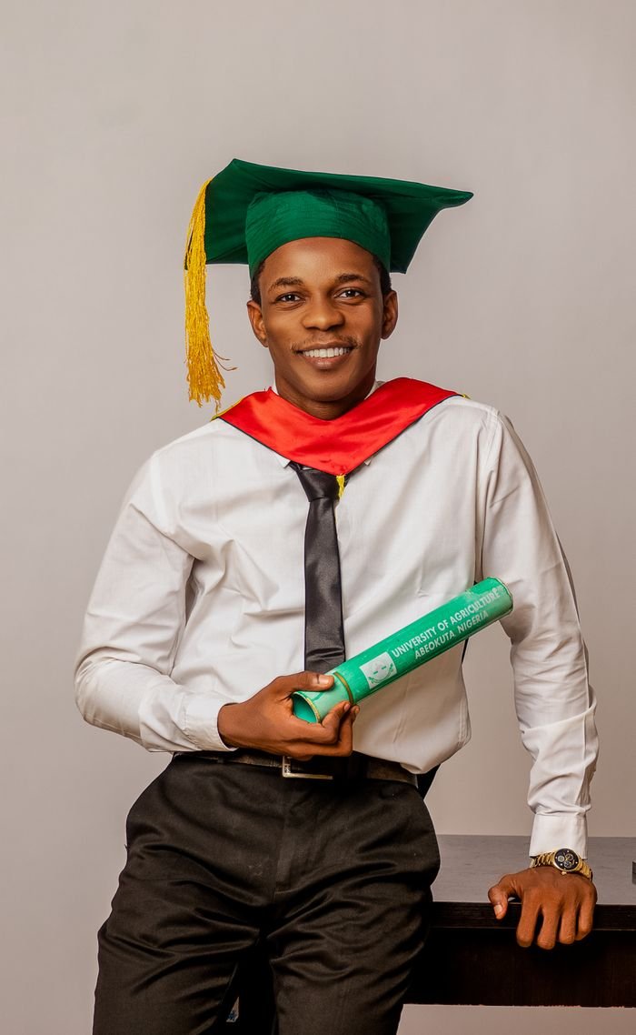 Confident young graduate in cap and gown holding diploma indoors.
