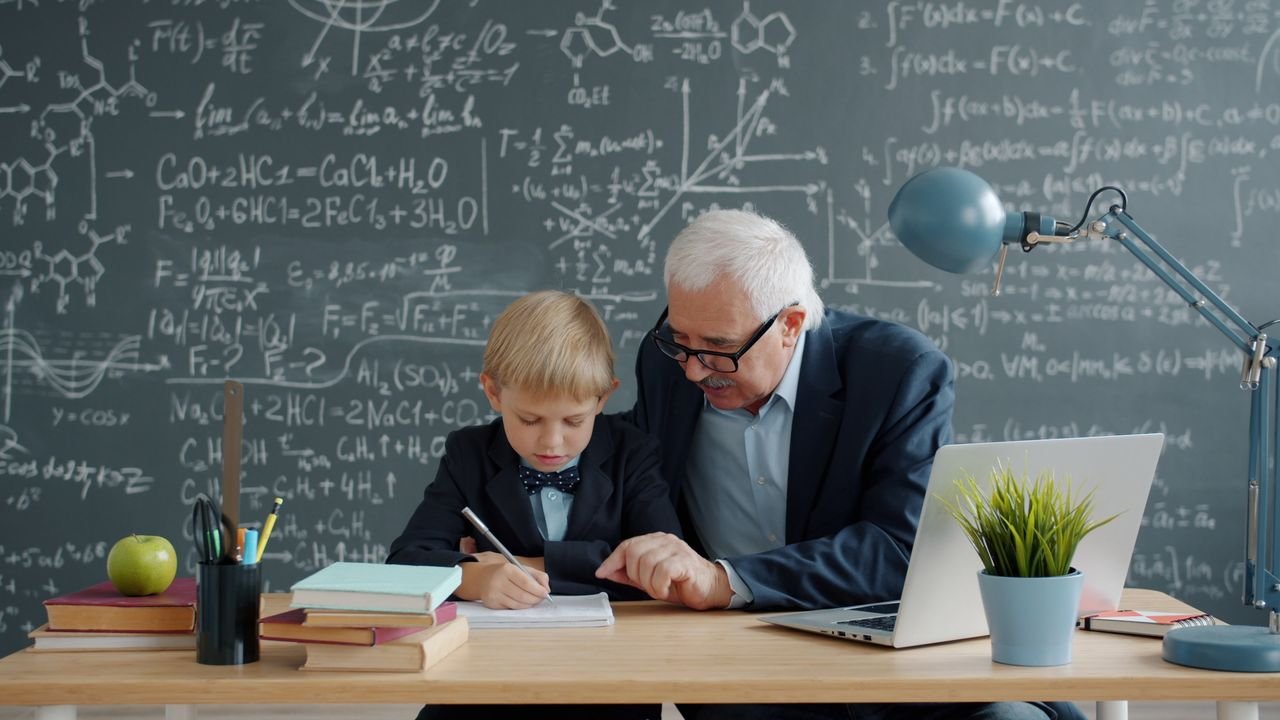 Elderly man teaching young boy with math on chalkboard background.