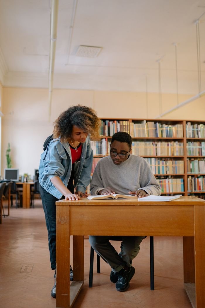 Two university students studying together in a library, focusing on textbooks and learning.